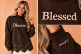 Close-ups of the approved ivory Blessed chest embroidery and covered-and-gold-cross wrist signature on smooth sleeve fabric, not ribbing.